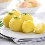 Stary przepis na pyzy ziemniaczane, podane na białym talerzu z natką pietruszki. Jedna pyza jest przekrojona.