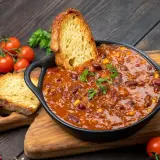 Pyszne dania na obiad: aromatyczne chili con carne z fasolą i kukurydzą, podane z chrupiącym pieczywem i świeżymi pomidorkami.