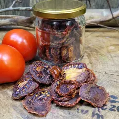 Słoik pełen aromatycznych suszonych pomidorów obok świeżych pomidorów i gałązek na drewnianym blacie.