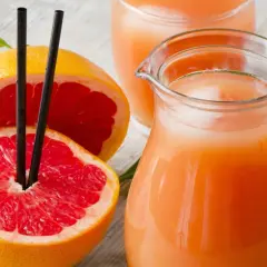 Orzeźwiający sok z grejpfruta w dzbanku i szklance, obok przekrojonych owoców. Idealny na letnie upały.