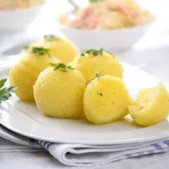Stary przepis na pyzy ziemniaczane, podane na białym talerzu z natką pietruszki. Jedna pyza jest przekrojona.