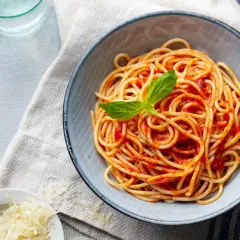 Misternie ułożone spaghetti z sosem pomidorowym i listkiem bazylii. Obok miseczka z tartym parmezanem. Idealne pytanie: jakie przyprawy do spaghetti?