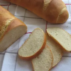 Chleb pszenny na zakwasie, pokrojony w kromki, leży na kratkowanym obrusie. Idealny do śniadania.