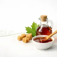 Czy syrop klonowy jest zdrowy? Na zdjęciu syrop klonowy w karafce i miseczce, obok kostki cukru i liść klonu.