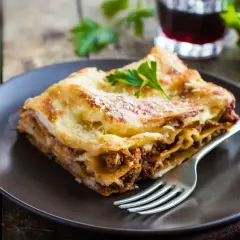 Pyszny kawałek lasagne z mięsem mielonym, idealny na prosty obiad. Posypana parmezanem i udekorowana natką pietruszki.