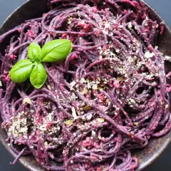 Fioletowy makaron z pesto ze słoika, posypany orzechami i udekorowany listkiem bazylii.