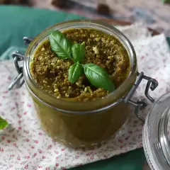Słoik z domowym pesto pistacjowym, ozdobiony listkami bazylii i posypany pistacjami.