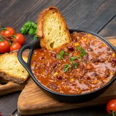 Pyszne dania na obiad: aromatyczne chili con carne z fasolą i kukurydzą, podane z chrupiącym pieczywem i świeżymi pomidorkami.