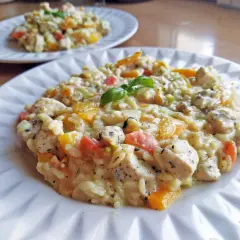 Szybkie risotto z warzywami i kurczakiem, udekorowane listkiem bazylii. Pyszne i kolorowe danie na talerzu.