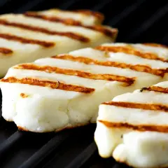 Trzy kawałki halloumi z grilla, z apetycznymi paskami, leżą na czarnej, grillowej powierzchni.