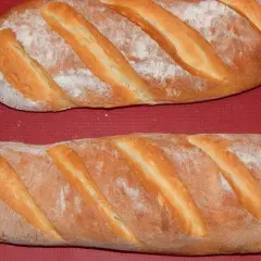Dwie świeże bułki wrocławskie, lekko oprószone mąką, leżą na czerwonym tle.