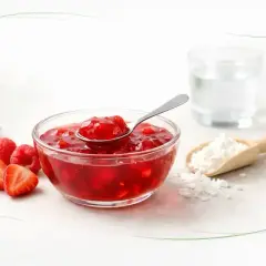 Czy kisiel jest zdrowy? Miseczka z czerwonym kisielem, maliny, truskawki, łyżeczka, szklanka wody i mąka ziemniaczana.