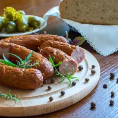 Pyszna kiełbasa z piekarnika, podana z chlebem i ogórkami, ozdobiona rozmarynem i pieprzem.