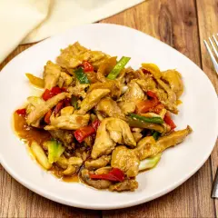 Pyszny kurczak shanghai z papryką i cebulką dymką w sosie na białym talerzu.