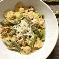 Pyszna pierś z kurczaka ze szparagami w sosie śmietanowym, podana z makaronem farfalle i posypana startym serem.