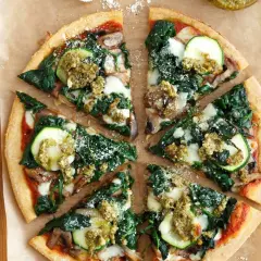 Pyszna pizza ze szpinakiem, cukinią i grzybami, polana sosem pesto.