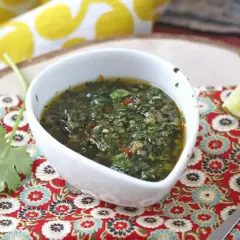 Aromaticzny sos chimichurri w białej miseczce, obok ćwiartka limonki i świeża kolendra.