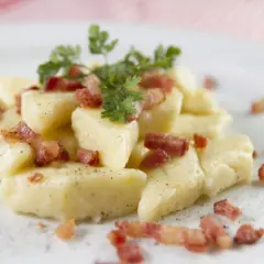 Kopytka z chrupiącym boczkiem i natką pietruszki, posypane pieprzem. Pyszne danie, które zadowoli każdego smakosza.