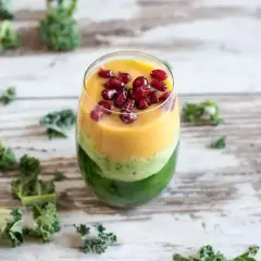Warstwowy koktajl z jarmużu, mango i granatu, ozdobiony pestkami granatu.