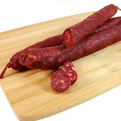 Trzy długie kiełbaski chorizo leżą na drewnianej desce. Jedna jest przekrojona, ukazując charakterystyczny, czerwony środek.