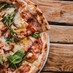 Pyszna pizza carbonara z chrupiącym boczkiem i rukolą, podana na drewnianym blacie.