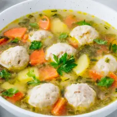 Zupa klopsowa babci: aromatyczny bulion z klopsikami, ziemniakami i marchewką, posypana natką pietruszki.
