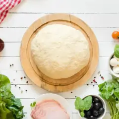 Świeże ciasto na pizzę czeka na składniki. Zastanawiasz się, ile może leżeć ciasto na pizze? Oto składniki na pyszną pizzę: pomidorki, mozzarella, oliwki, bazylia, szynka.