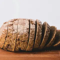 Kromka chleba razowego na desce. Zastanawiasz się, ile kalorii ma kromka chleba z masłem?