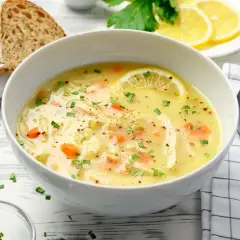 Aromatyczna zupa cytrynowa z kurczakiem, marchewką i makaronem, ozdobiona plasterkiem cytryny i natką pietruszki. Podana z chlebem.
