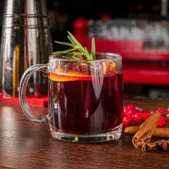 Aromatyczny grog z pomarańczą i rozmarynem, ozdobiony laskami cynamonu i gwiazdkami anyżu, kusi na drewnianym blacie.