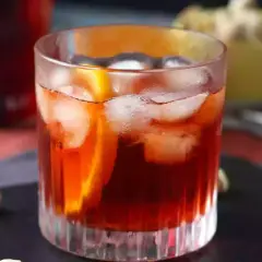 Klasyczny negroni przepis: czerwony koktajl z lodem i pomarańczą w szklance, obok pistacje.