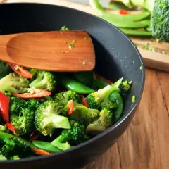 Brokuły, groszek cukrowy i papryczka chili w woku, gotowe do stir fry. Drewniana łopatka miesza warzywa.