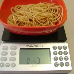Porcja makaronu w czerwonej misce na wadze cyfrowej. Waga pokazuje 0.43 funta, co pomaga w ustaleniu, jak liczyć kalorie makaronu.