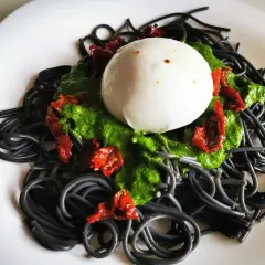 Czarny makaron z zielonym pesto, suszonymi pomidorami i kulką mozzarelli. Pyszne danie, które zachwyca wyglądem i smakiem.