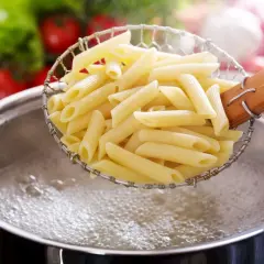 Penne w cedzaku, gotowe do podania, idealnie ugotowane makaron al dente. W tle pomidory i sałata.
