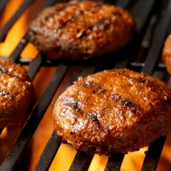 Soczyste burgery z grilla pieką się na rozżarzonych węglach, tworząc apetyczne paski.