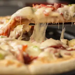 Gorąca, ciągnąca się pizza mrożona z serem, szynką i ananasem. Kawałek pizzy jest podnoszony, odsłaniając roztopiony ser.