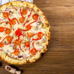 Apetyczna pizza capricciosa z pomidorkami, papryką i serem na drewnianym blacie.
