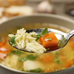 Łyżka pełna makaronu, marchewki i pietruszki z aromatycznego rosołu z pieczonych warzyw.