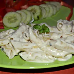 Penne w kremowym sosie z mozzarellą, udekorowane bazylią. Obok plasterki ogórka i papryka.