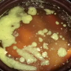 Gęsta, zielona piana na powierzchni aromatycznej zupy na rosole. Widać kawałki warzyw i mięsa.