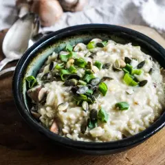 Aksamitne risotto z pieczarkami, posypane pestkami dyni i szczypiorkiem, czeka na talerzu.