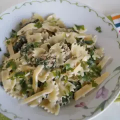 Pyszny makaron farfalle z tuńczykiem i szpinakiem, posypany świeżą natką pietruszki.