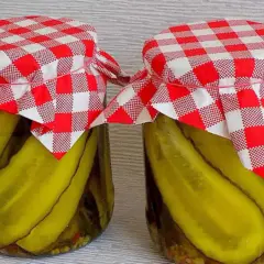 Słoiki z ogórkami w curry ze skórką, ozdobione czerwono-białymi kratkowanymi chusteczkami.