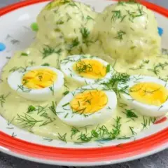 Pyszne jajka w sosie chrzanowym, udekorowane świeżym koperkiem, podane na talerzu z kolorowymi kropkami.