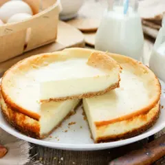 Pyszny sernik z kawałkiem na wierzchu, obok mleko i jajka. Czy sernik można zamrozić? Tak, ten wygląda idealnie do mrożenia!