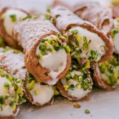 Słodkie rurki wypełnione kremowym serek ricotta, posypane cukrem pudrem i pistacjami. Pyszna włoska przekąska.