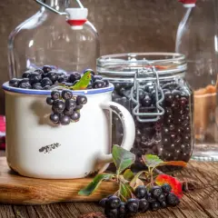 Aronia w słoiku i kubku, gotowa na nalewkę z aronii przepis babci. Obok puste butelki.