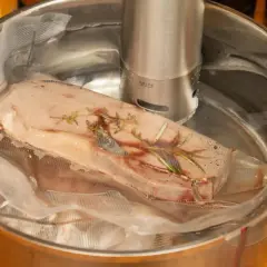 Mięso w woreczku z ziołami, zanurzone w wodzie z cyrkulatorem sous vide.