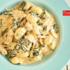 Pyszne gnocchi z kurczakiem i szpinakiem w kremowym sosie, posypane parmezanem. Danie wygląda apetycznie i zachęca do spróbowania.